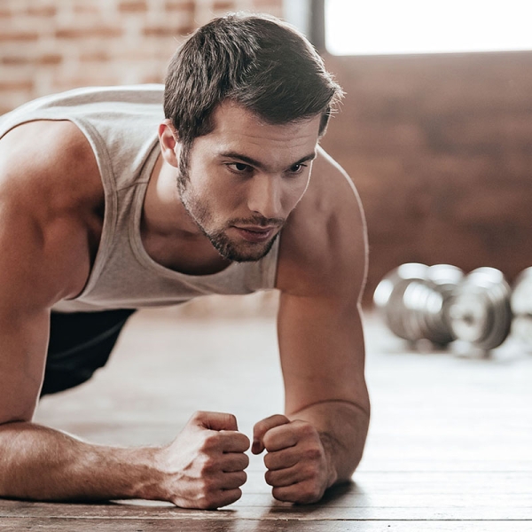 Confident muscled young man wearing sport wear and doing plank position while exercising on the floor in loft interior